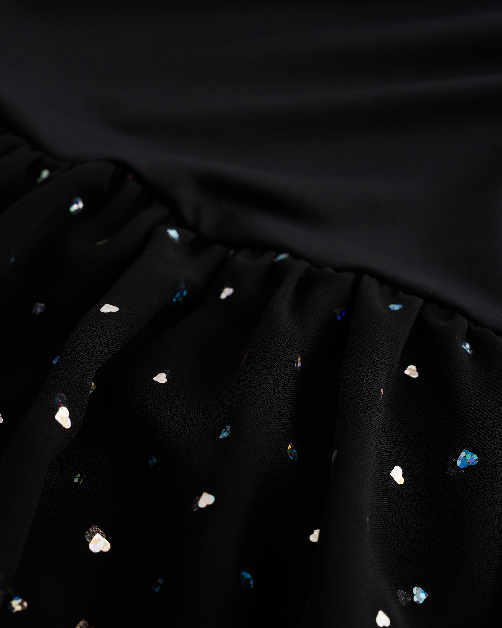 Close-up of black sequin dress showing heart-shaped sequins, chiffon skirt fabric, and gathered waist detail.
