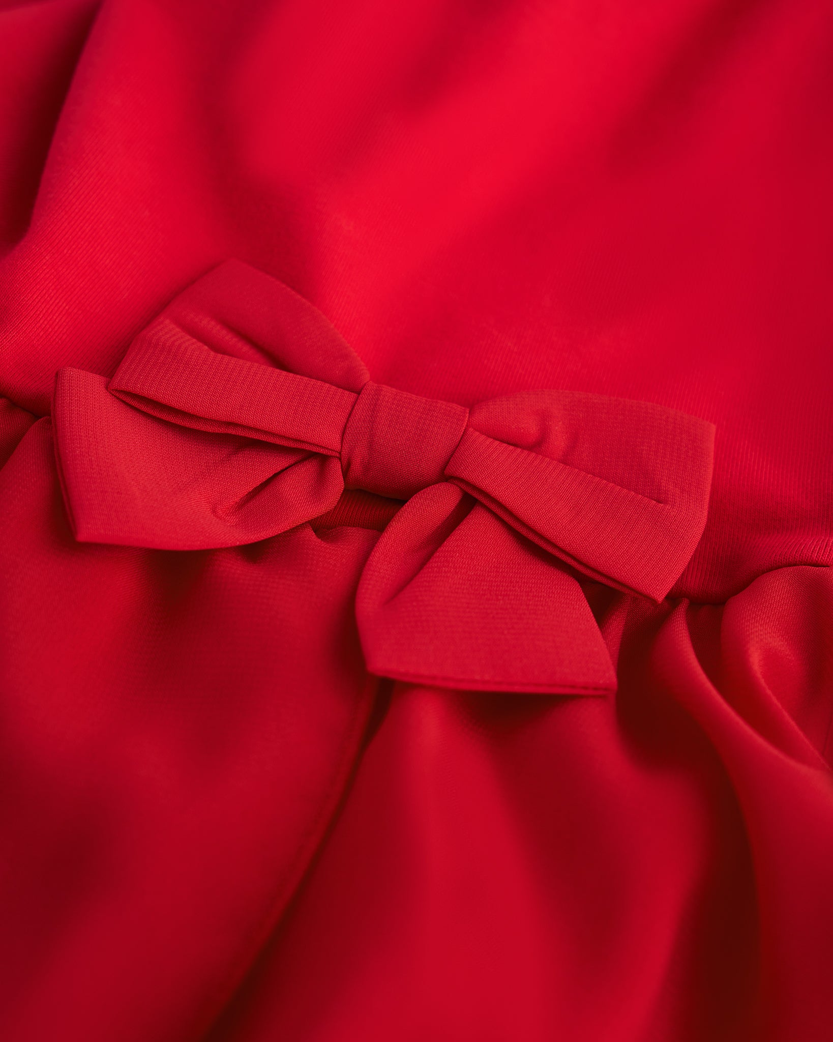 Close-up of red ballet dress showing the decorative bow accent and soft chiffon wrap skirt.