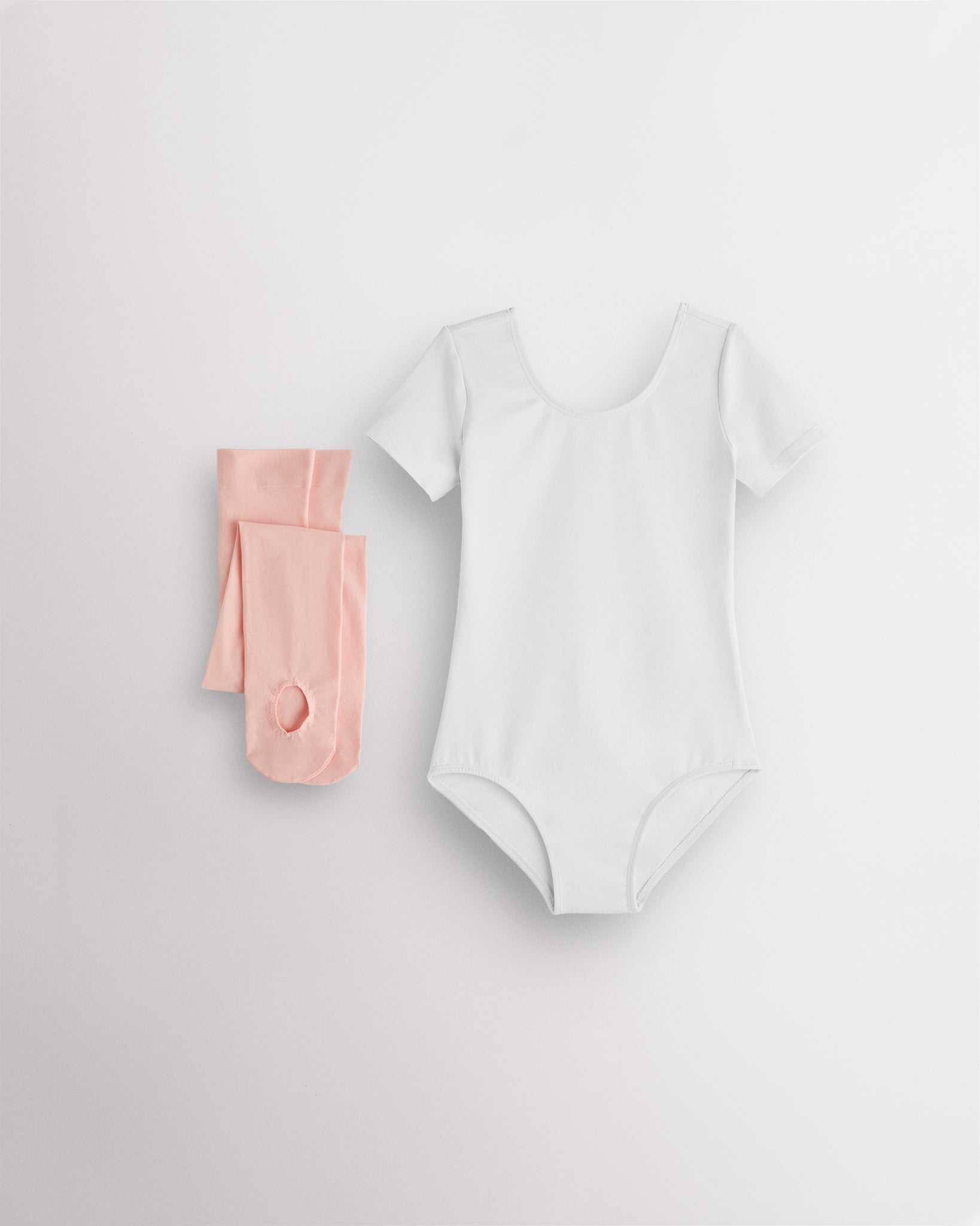 White short sleeve leotard with pink convertible dance tights laid flat for girls ballet and dance class.