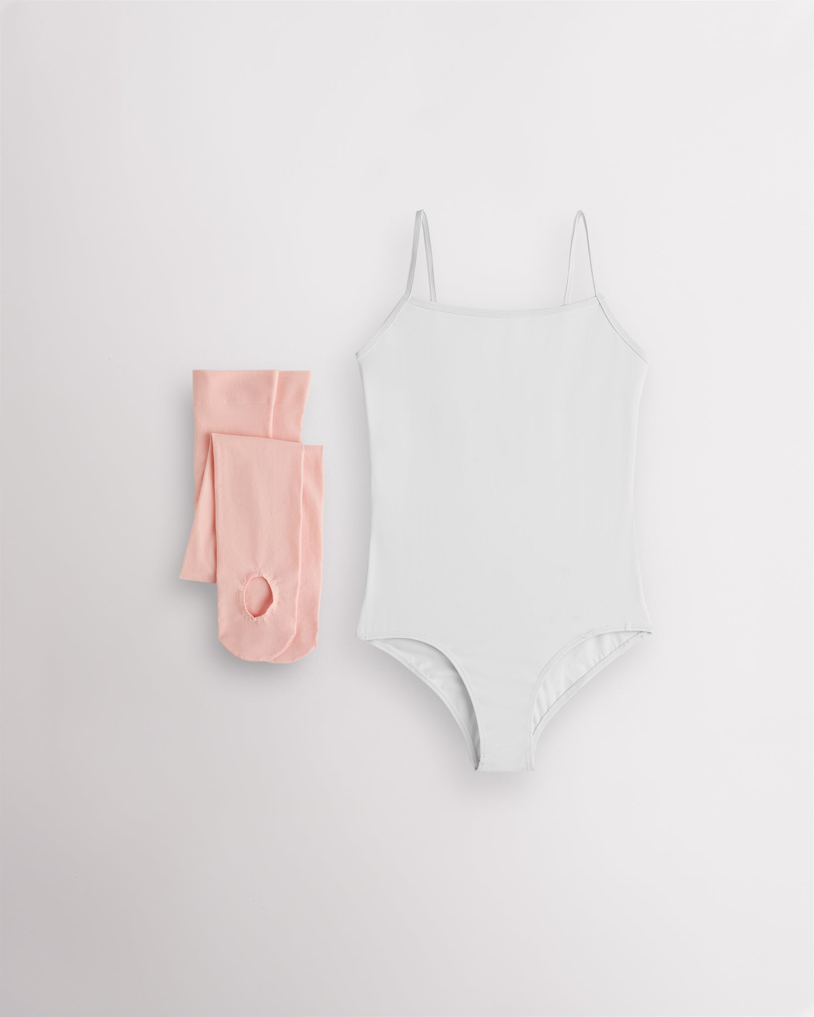 White girls camisole leotard with pink convertible dance tights laid flat for ballet and dance class.