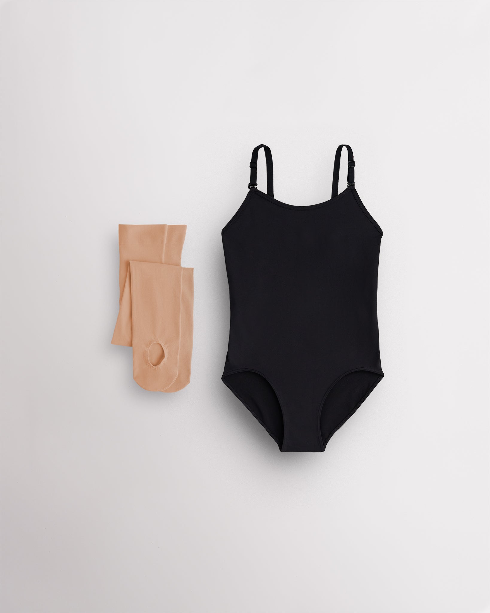 Black camisole leotard for girls with tan convertible tights laid flat for ballet, dance, and costume layering.