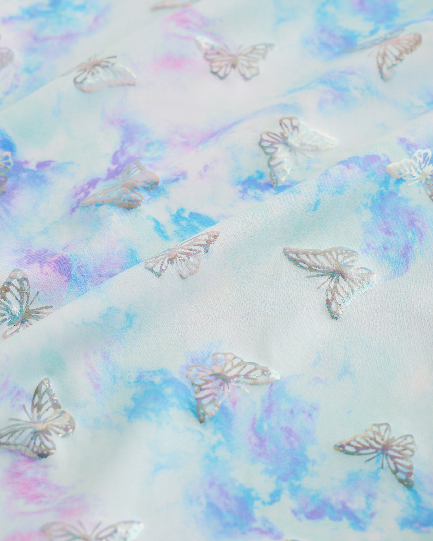 Close-up of Butterfly Mist girls unitard fabric showing butterflies, rainbows, moons, stars, and soft shimmer detail.