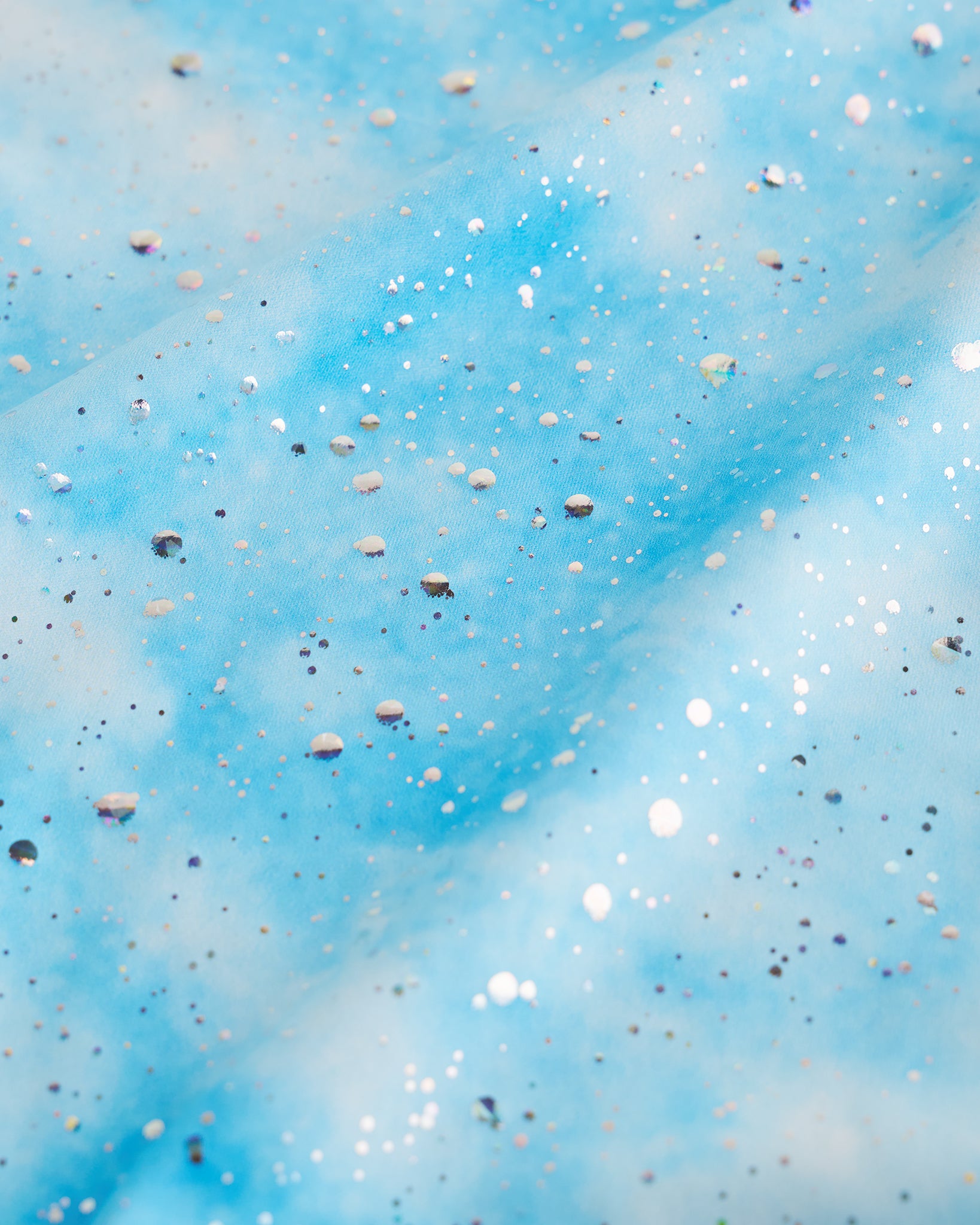 Close-up of Cloudburst Blue girls unitard fabric showing butterflies, rainbows, moons, stars, and soft shimmer detail.