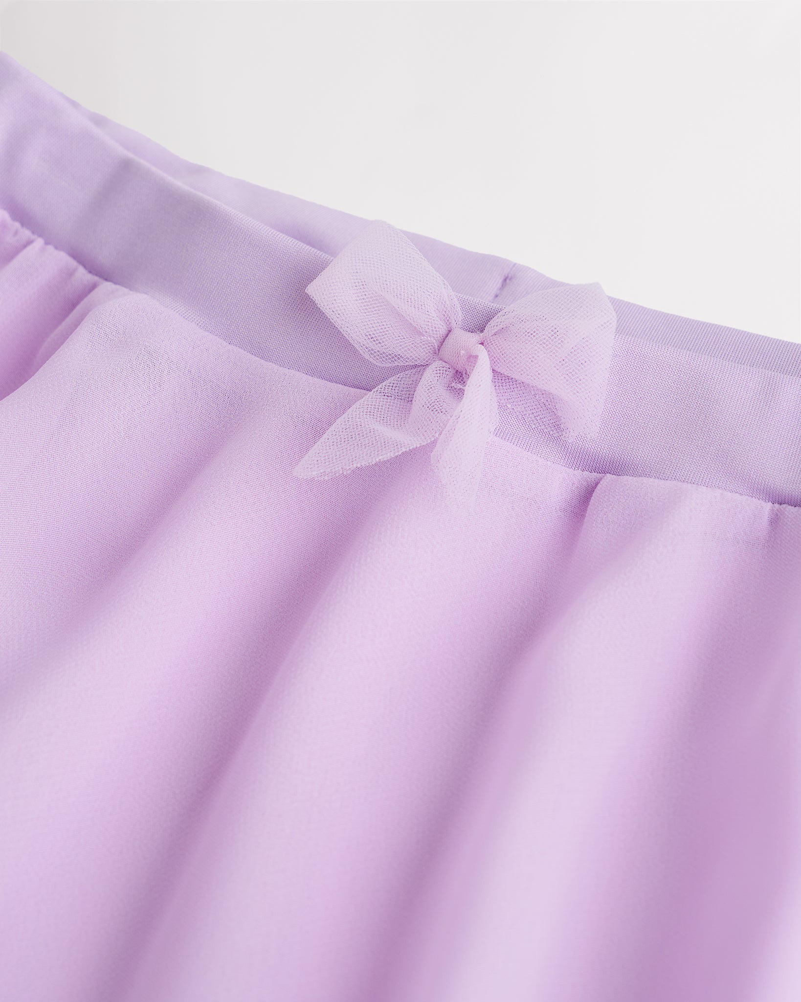 Close-up of a girls lavender chiffon ballet skirt showing the soft elastic waistband and delicate bow detail at the waist.