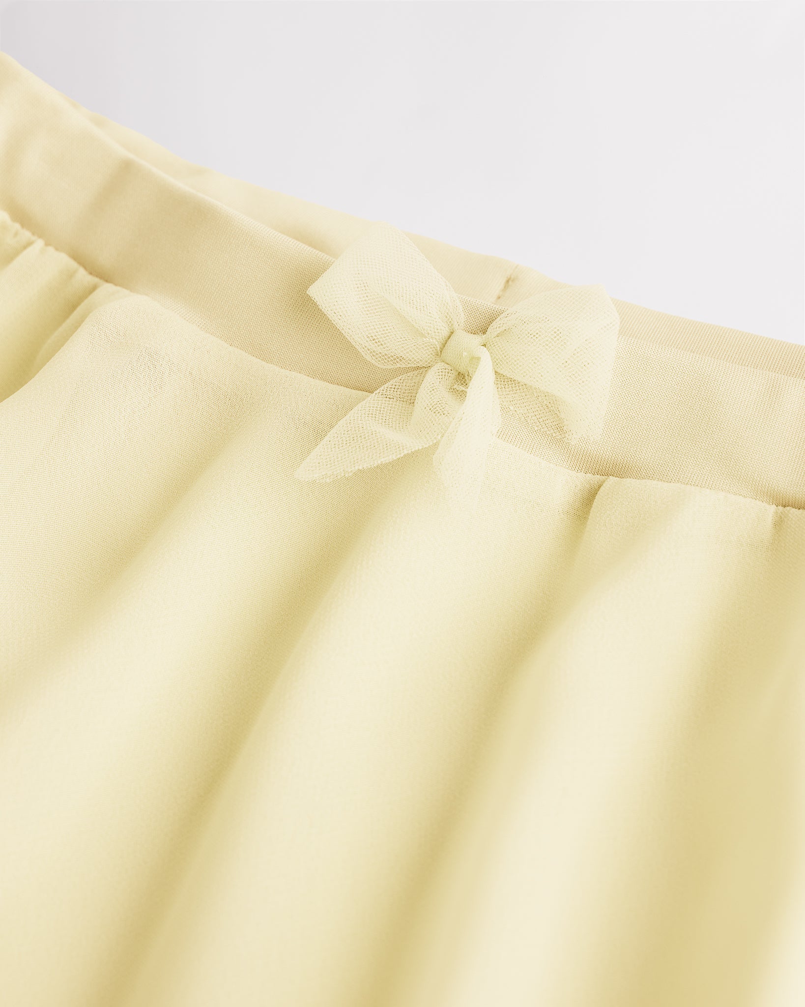 Close-up of a girls lemon butter chiffon ballet skirt showing the soft elastic waistband and delicate bow detail at the waist.