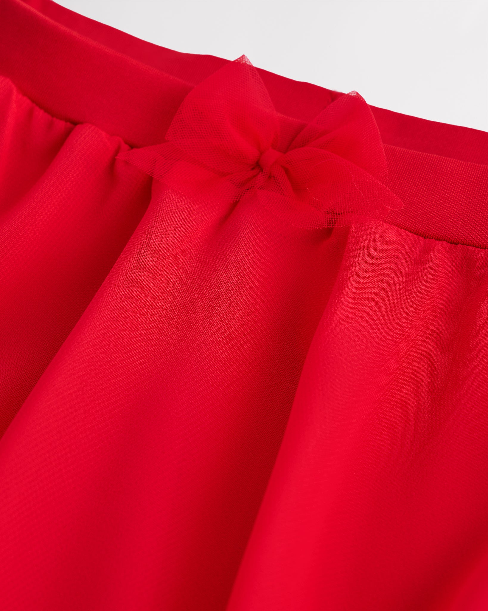 Close-up of a girls red chiffon ballet skirt showing the soft elastic waistband and delicate bow detail at the waist.