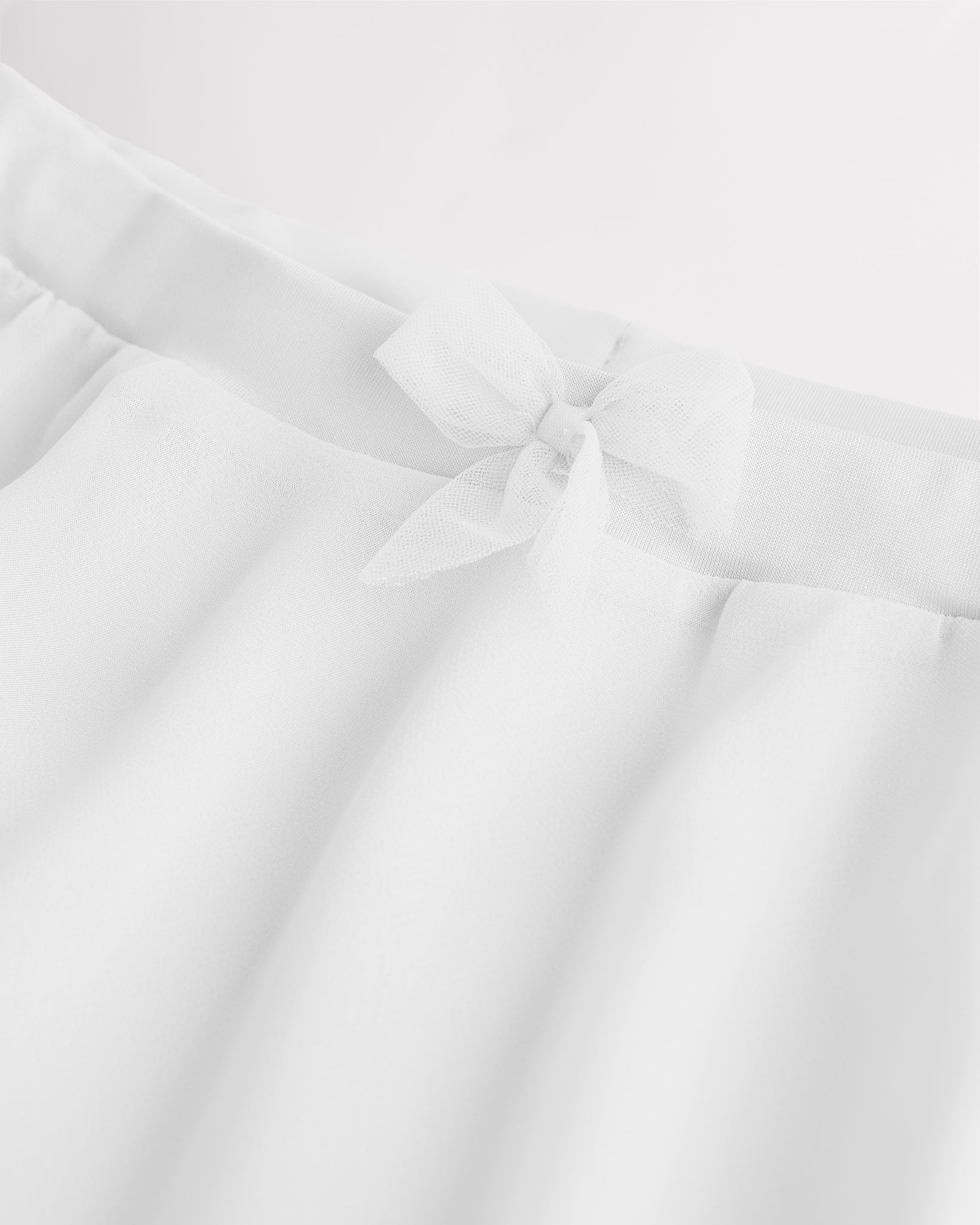Close-up of a white chiffon ballet skirt showing the soft elastic waistband and delicate bow detail at the waist.