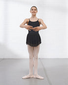 Young ballerina wearing a black leotard and black mesh ballet skirt with pink tights and ballet slippers in a studio.