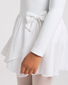 Close-up of white girls dance dress showing the bow accent, layered chiffon wrap skirt, and smooth long sleeve bodice.