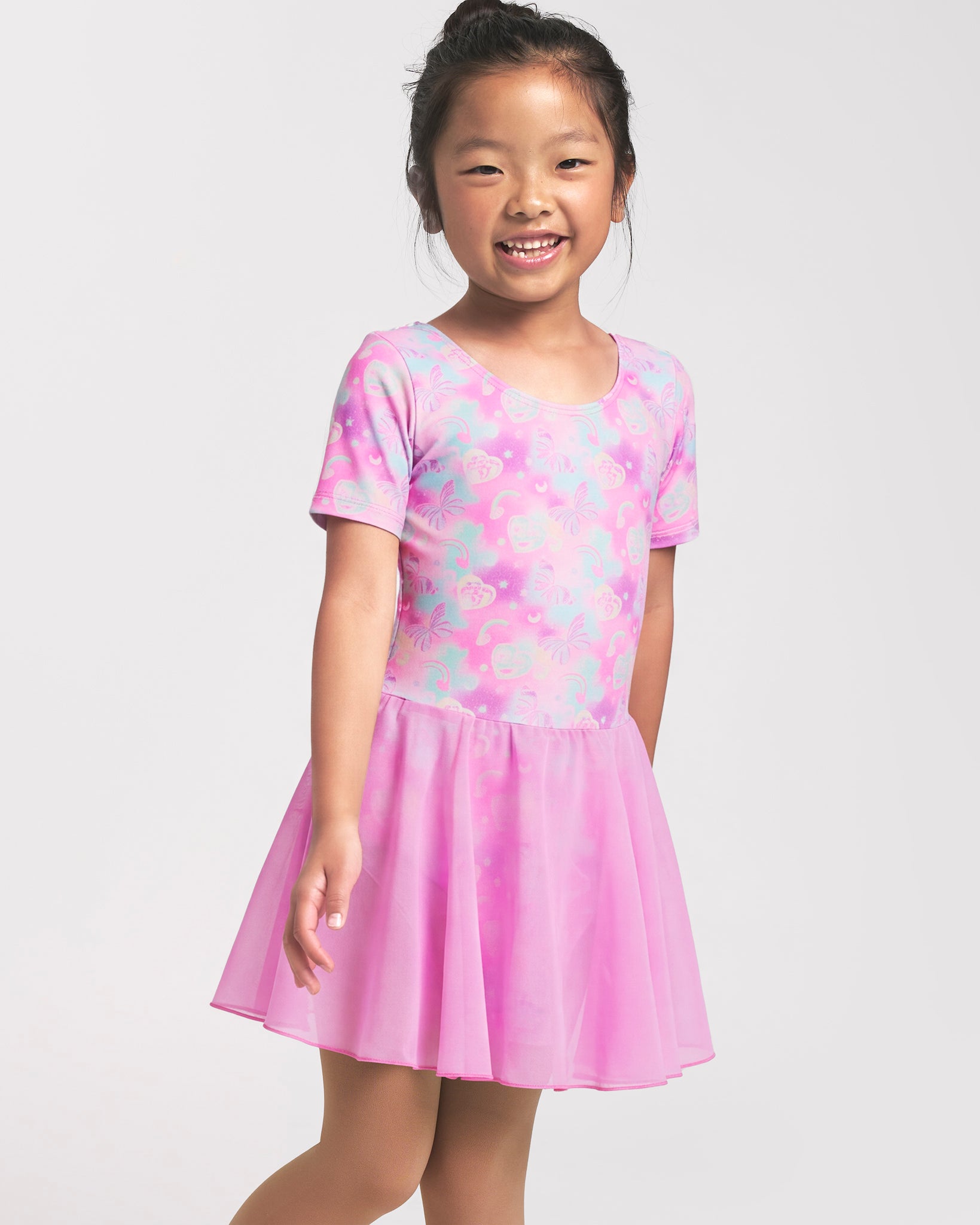 Girl wearing a Bow Dreams ballet dress with short sleeves, attached skirt, and colorful shimmering print.