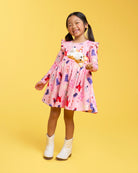 Girl wearing a Puppy Parade on Pink long sleeve dress with ruffle shoulders, gathered waist, A-line skirt, and white shoes.