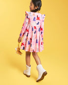 Back view of girl wearing a Puppy Parade on Pink girls dress with long sleeves, gathered waist, and playful allover puppy print.