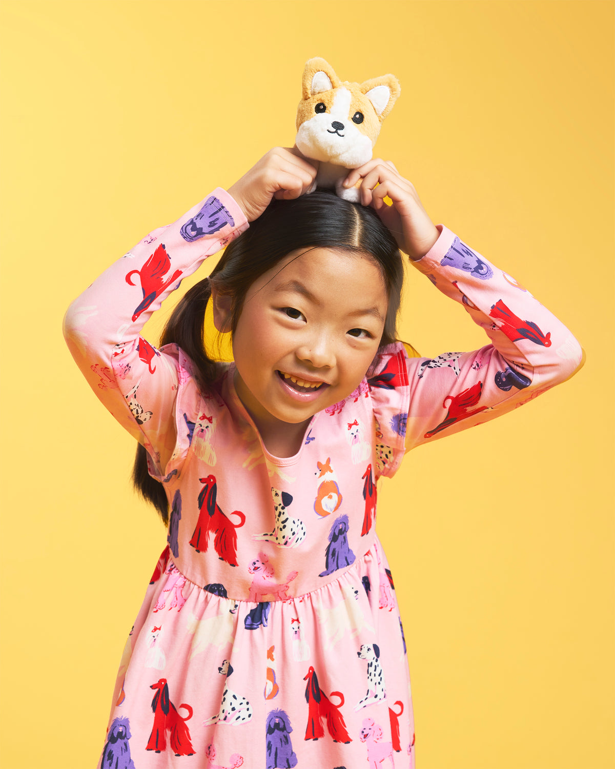 Close-up of girl wearing a Puppy Parade on Pink long sleeve print dress showing ruffle shoulder details and colorful in-house puppy graphics.