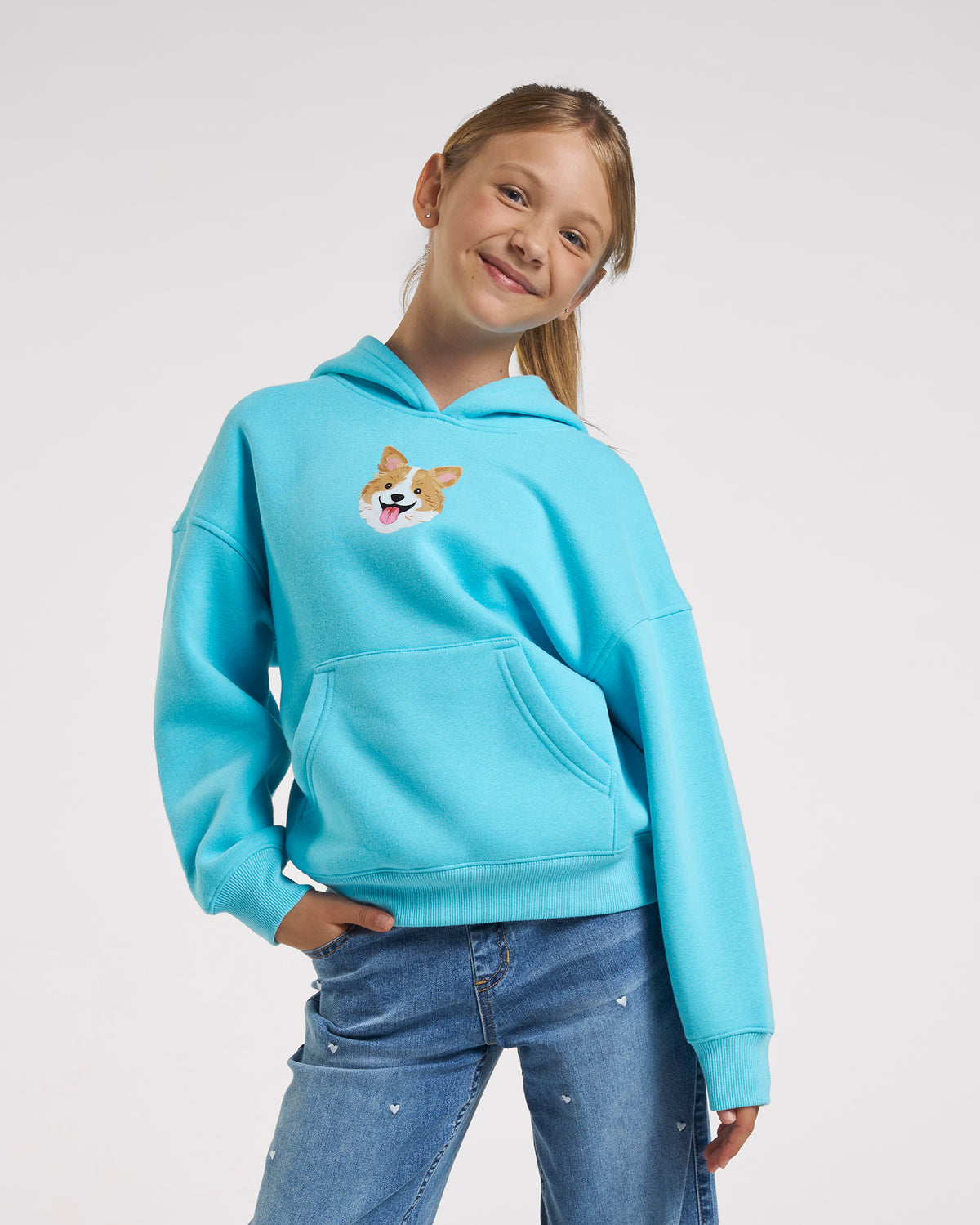 Girl wearing an aqua blue oversized corgi hoodie with fleece lining, kangaroo pocket, ribbed trim, and puppy graphic on the front.