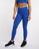 Blue high-waisted leggings with side pockets, contour seam details, and full-length fit styled with black sneakers.