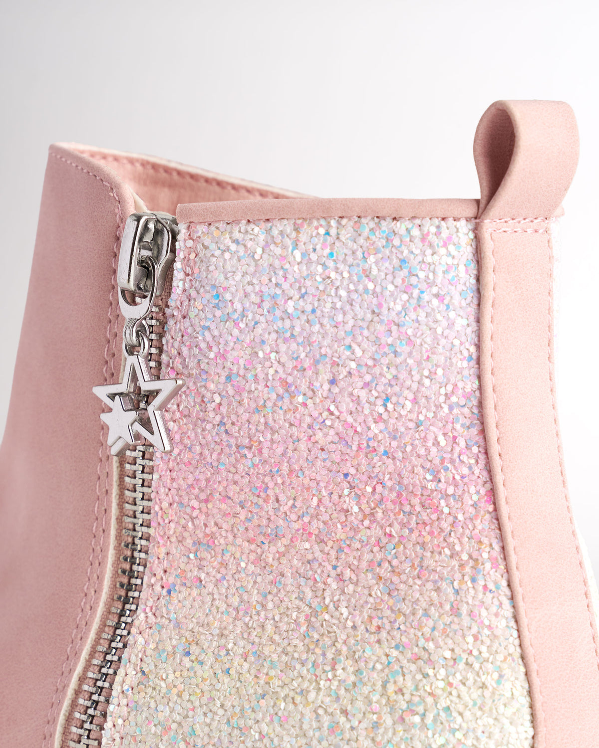 Close-up of a pink kids ankle boot's iridescent glitter heel panel, silver zipper with star charm and heel pull tab