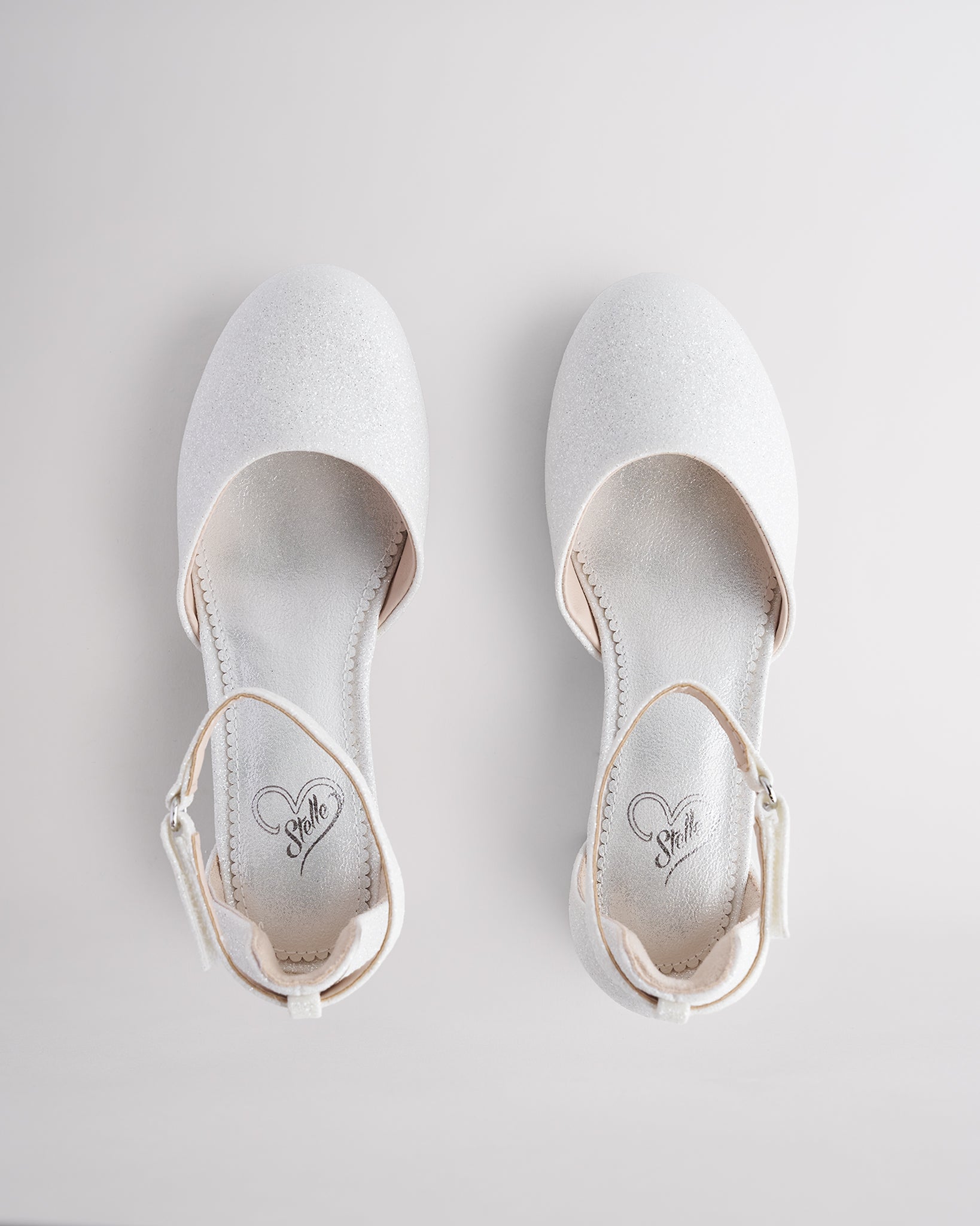Girls’ white glitter dress shoes with a low block heel and ankle strap.