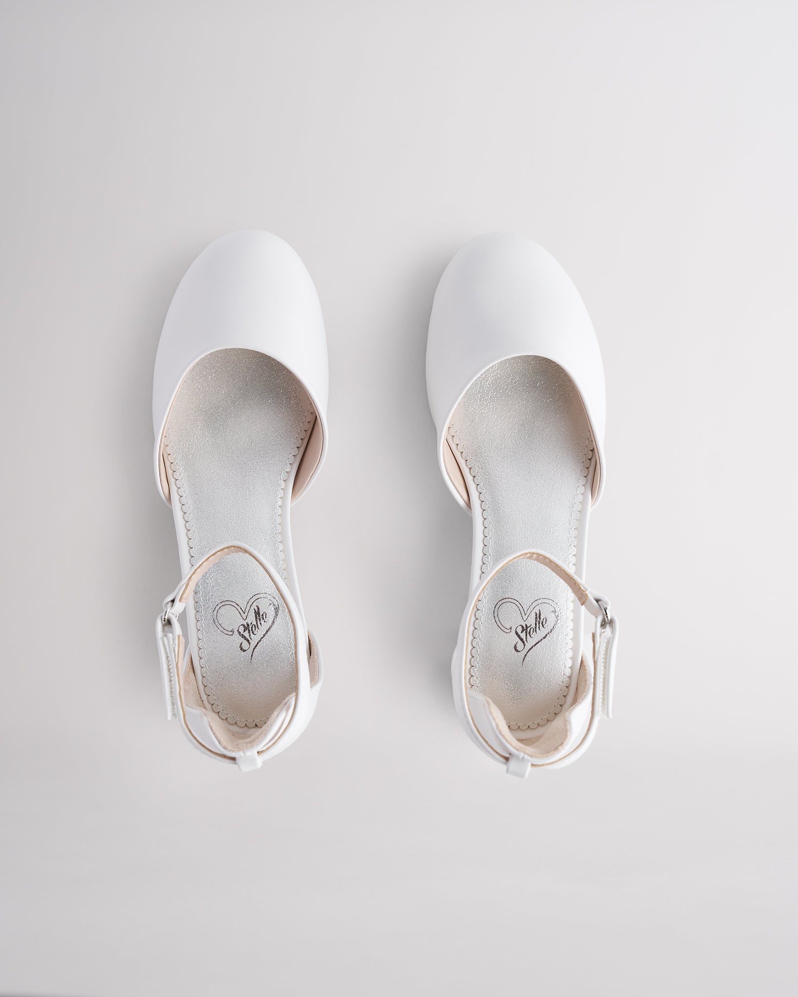 Girls’ white dress shoes with a low block heel and ankle strap.