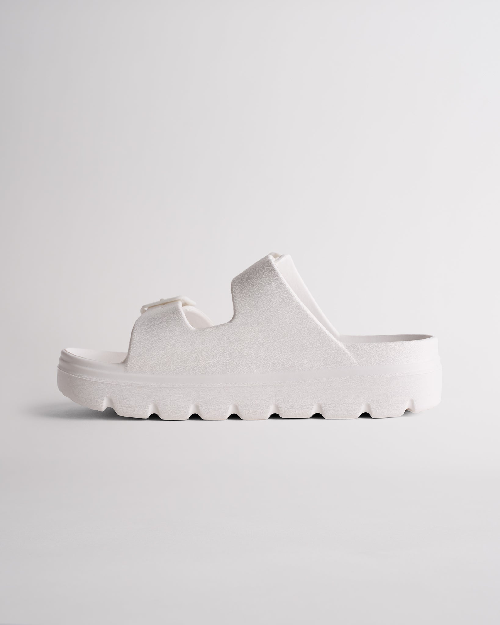 Side view of white Stelle Kids StelleCloud Buckled Slide showing the easy slide-on design, raised sole, and adjustable straps.