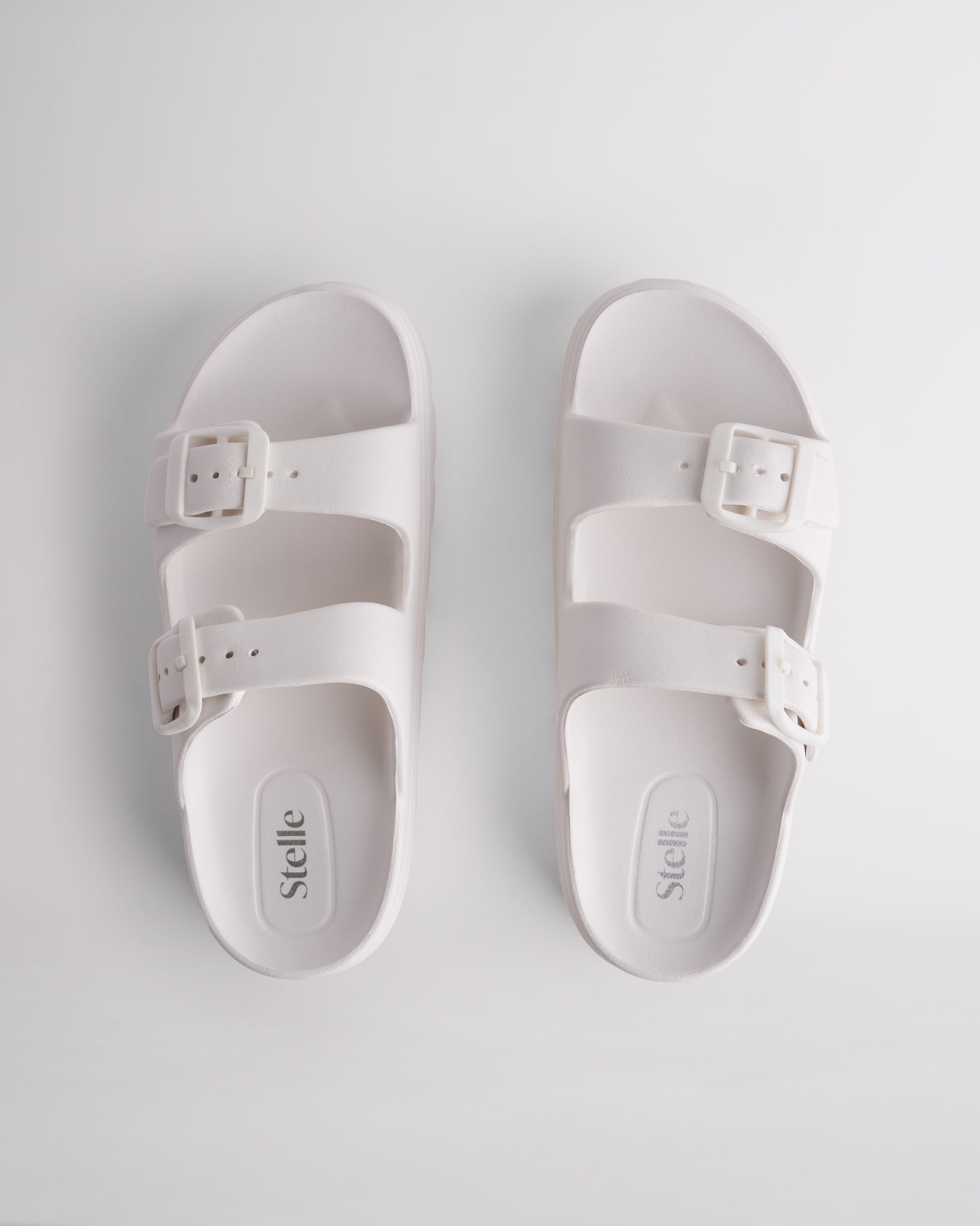 Top view of white Stelle Kids StelleCloud Buckled Slide with two buckle straps, contoured footbed, and Stelle logo detail.