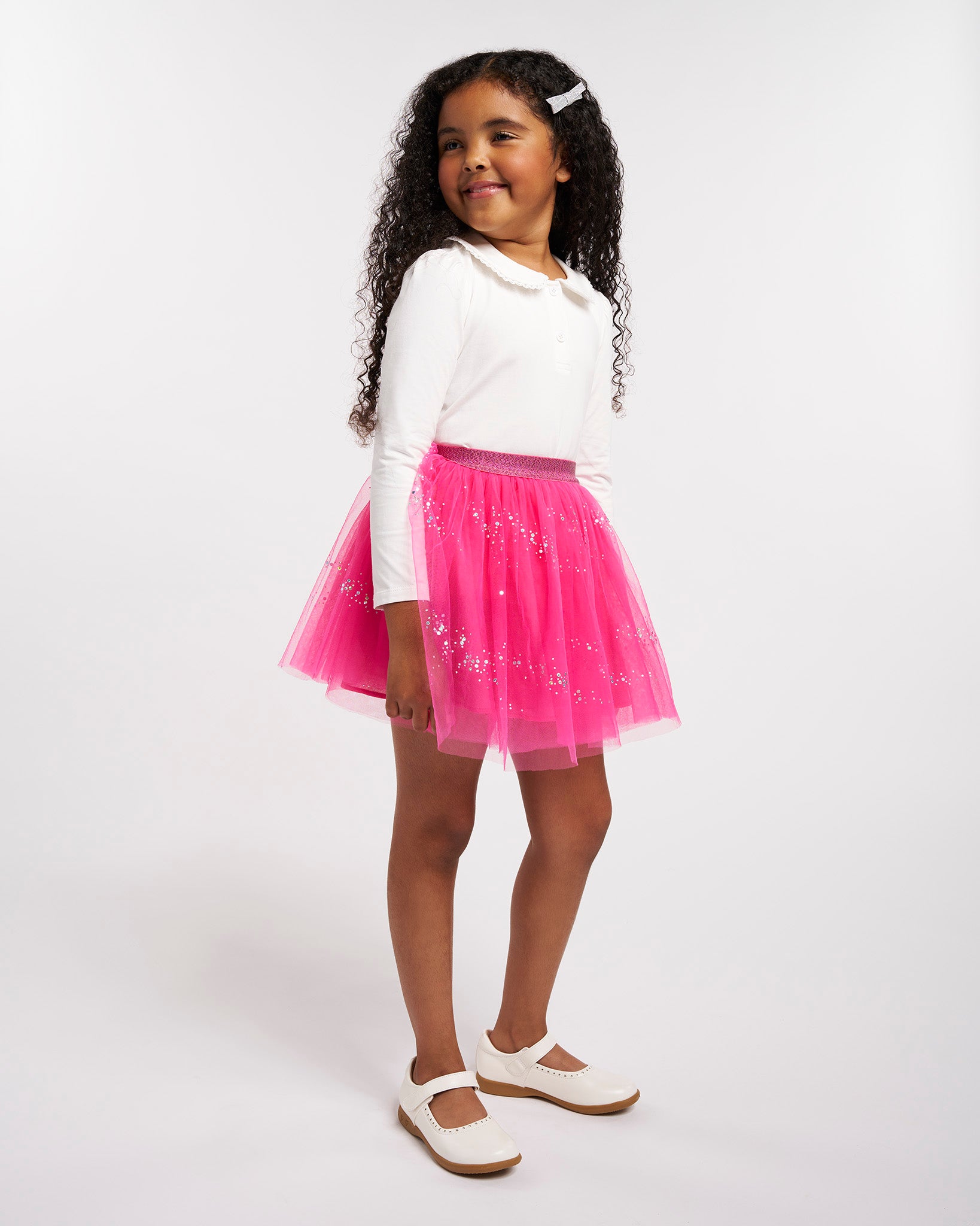 Girl wearing a white Peter Pan collar long sleeve top styled with a pink tulle skirt and Mary Jane shoes.