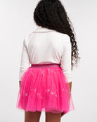 Back view of girl wearing a white long sleeve top with Peter Pan collar and pink sequin skirt.