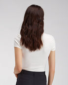 Person wearing a white shirt and black pants with long dark hair on a plain background