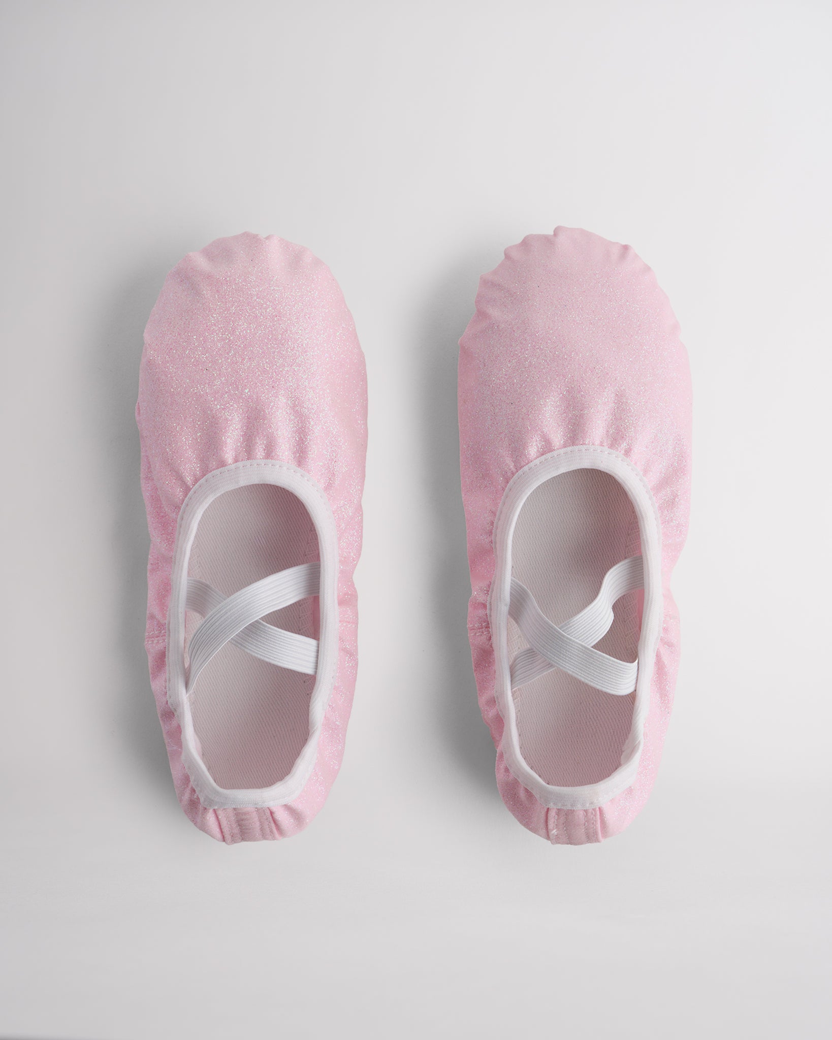 Kids glitter ballet shoes in pink glitter with crisscross elastic straps, top view