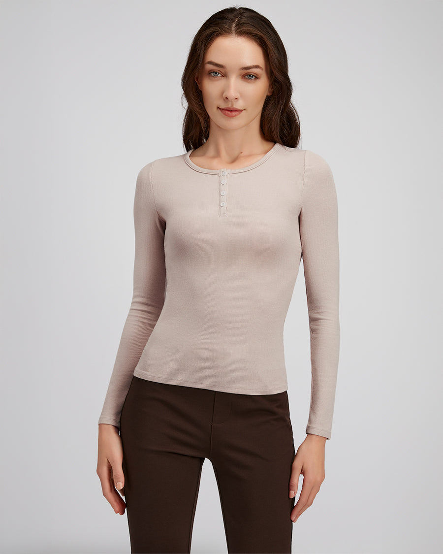 Woman wearing a beige long-sleeve top and brown pants on a light gray background