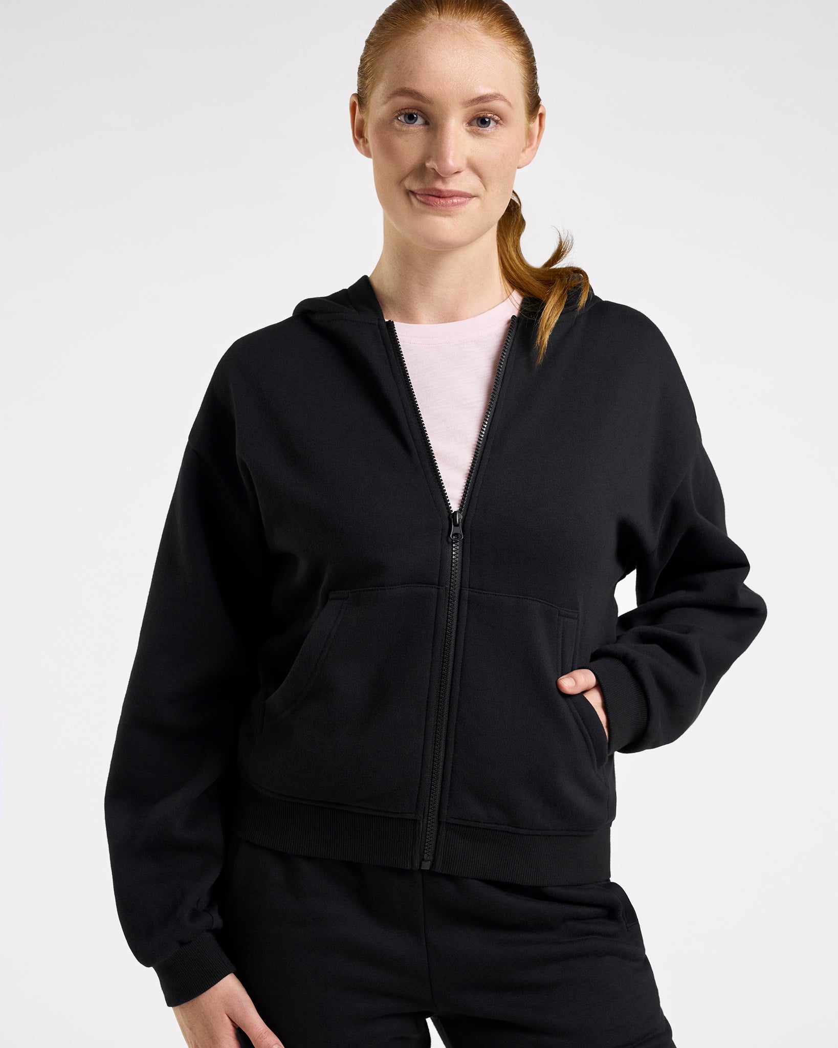 Woman wearing the black Stelle fleece-lined zip-up hoodie, front view with one hand in the kangaroo pocket.