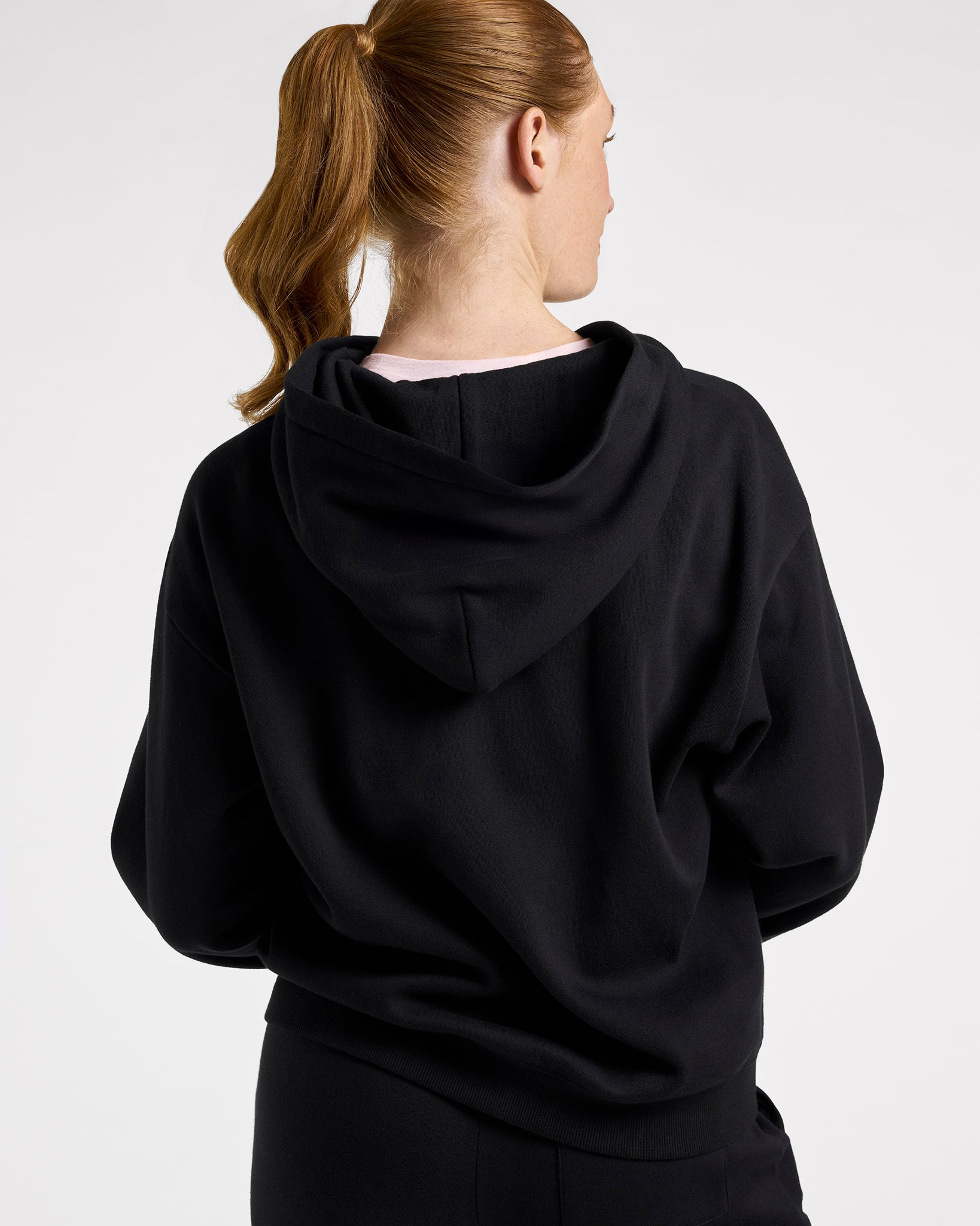 Back view of a woman wearing the black Stelle fleece-lined zip-up hoodie with the hood down.