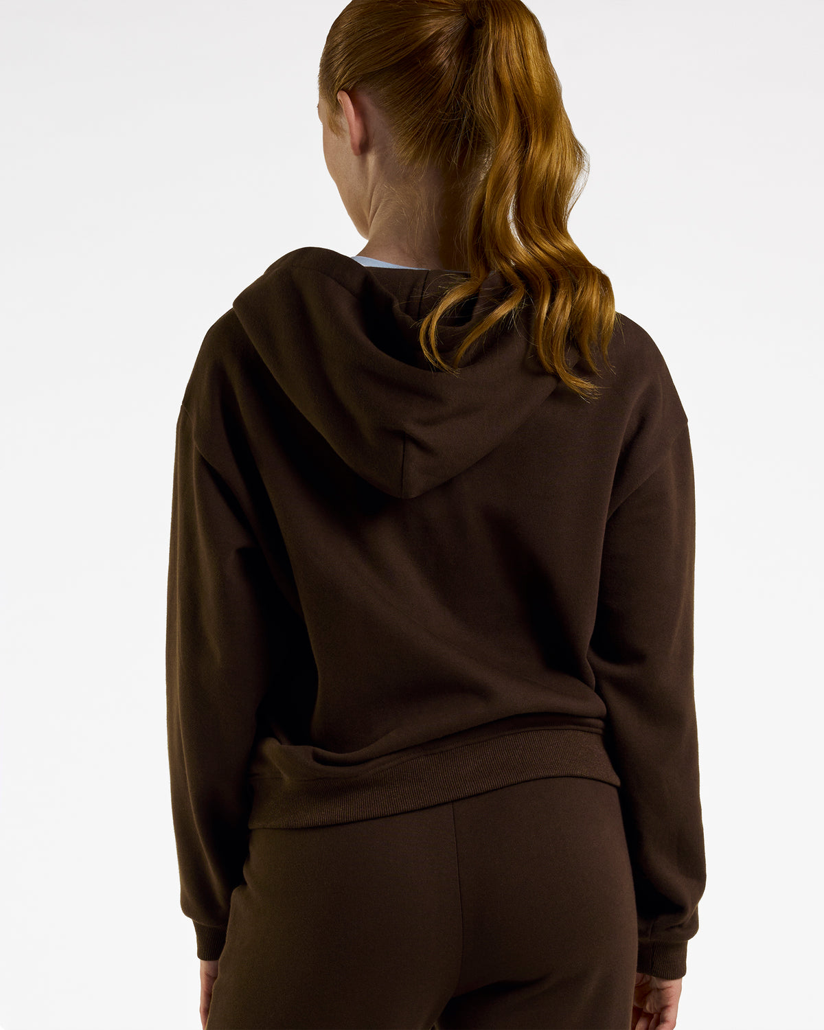 Back view of a woman wearing the brown Coffee Stelle fleece-lined zip-up hoodie with the hood down.