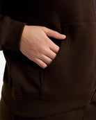 Close-up of a hand in the kangaroo pocket of the brown Coffee fleece-lined zip-up hoodie.