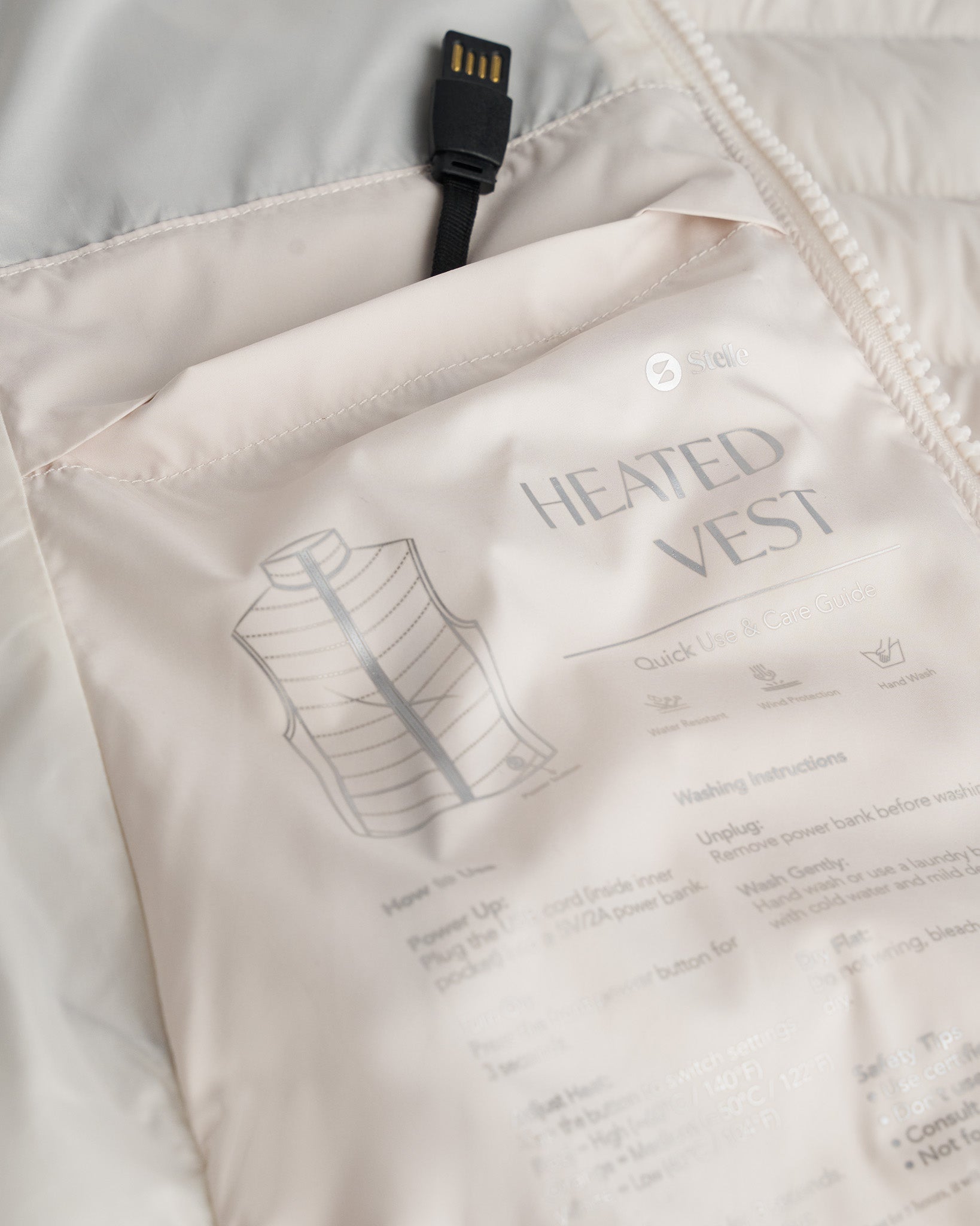 Close-up of a beige heated vest with text and a USB cable.