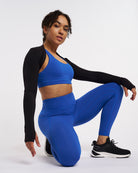 Model wearing black Stelle womens long sleeve shrug with thumb holes over a blue workout set