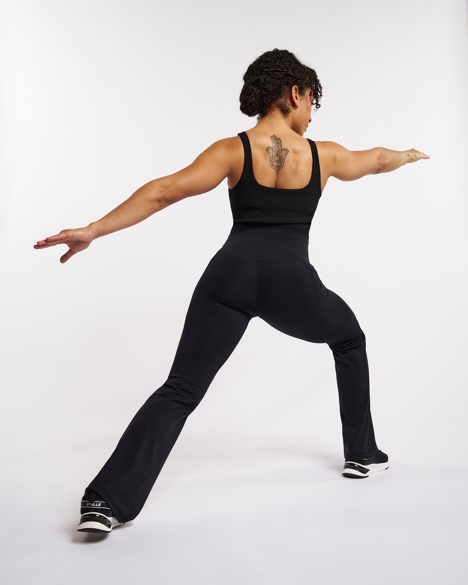 Model wearing black Stelle flare leggings with pockets in a workout pose, showing flexible fit and flared legs