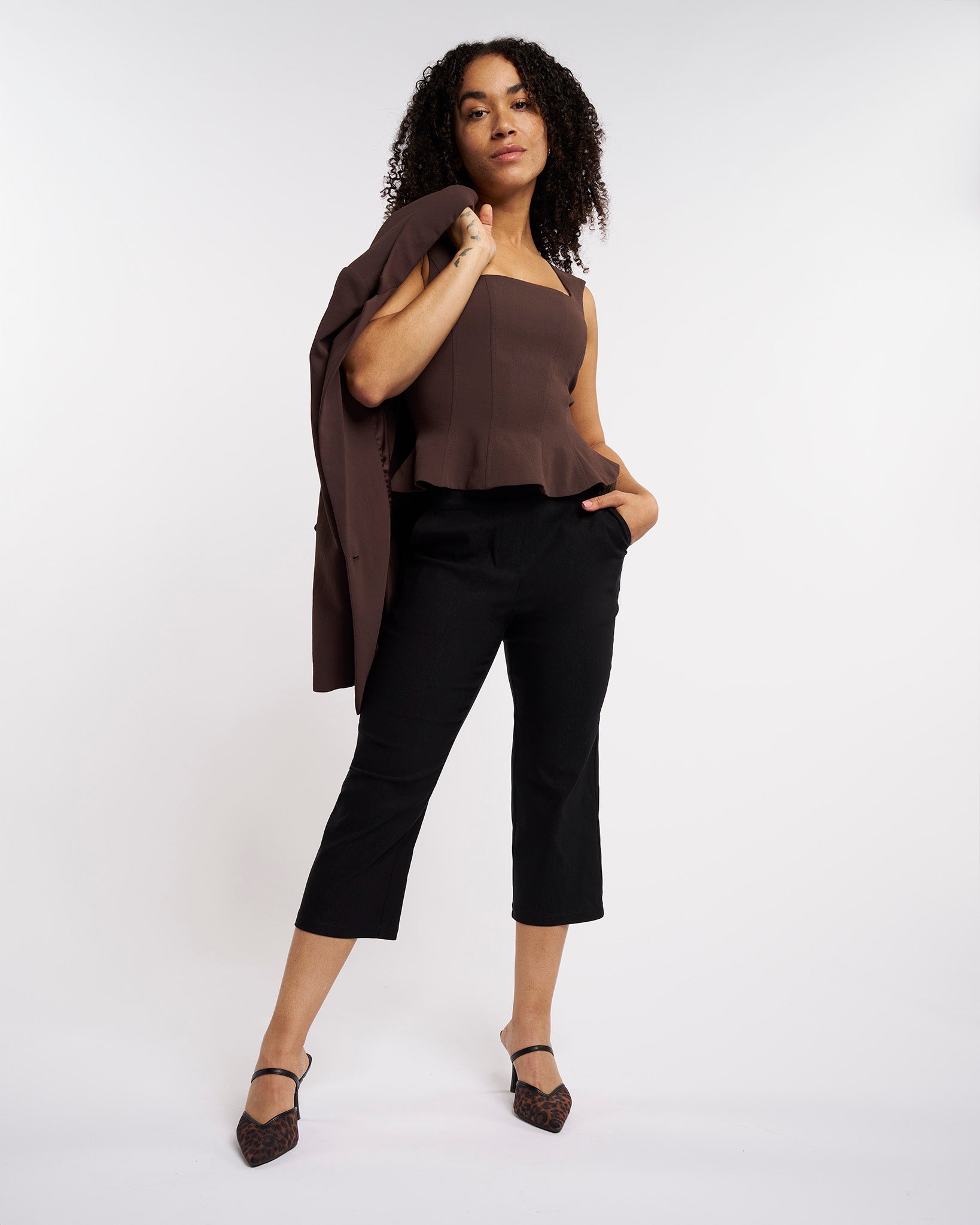 Woman styling black high-rise capri pants with a brown top and blazer for a polished casual look.
