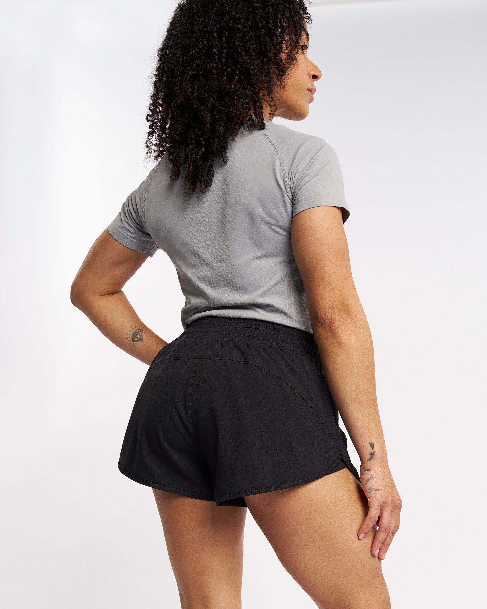 Back view of woman wearing black running shorts with a subtle back seam and relaxed outer layer.