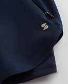 Close-up of navy Stelle gym shorts showing zipper pocket, curved hem stitching, and smooth performance fabric.