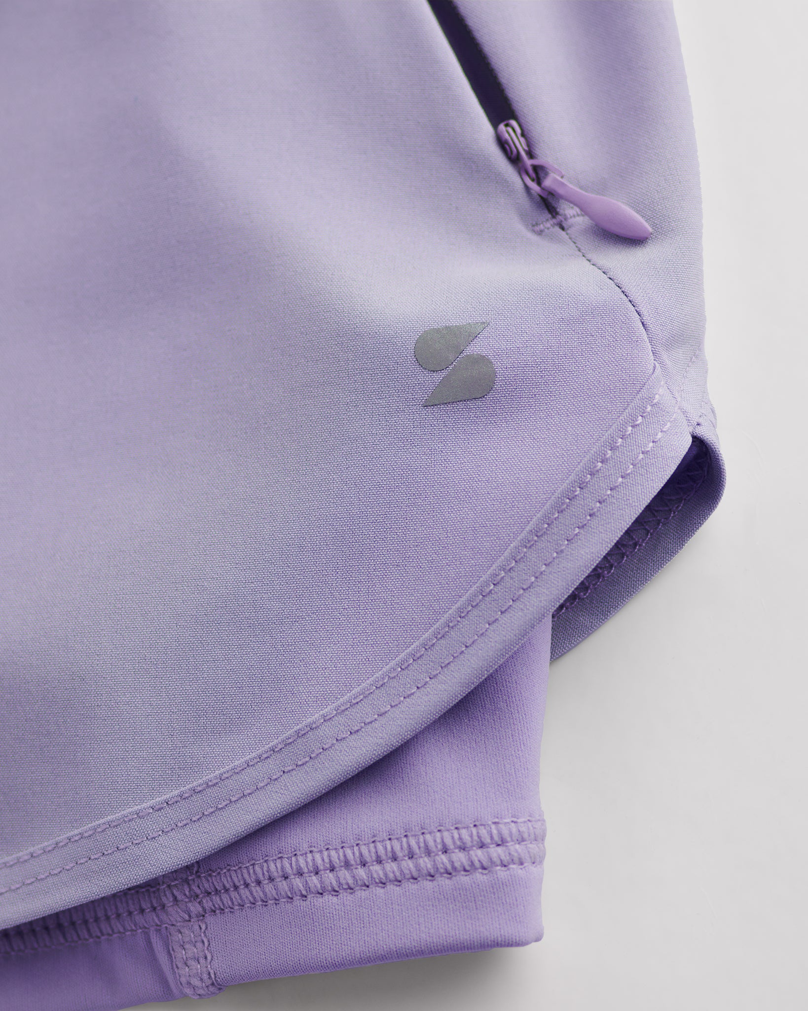 Close-up of Purple Haze Stelle gym shorts showing zipper pocket, curved hem stitching, and smooth performance fabric.