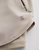 Close-up of Sandy Grey Stelle gym shorts showing zipper pocket, curved hem stitching, and smooth performance fabric.