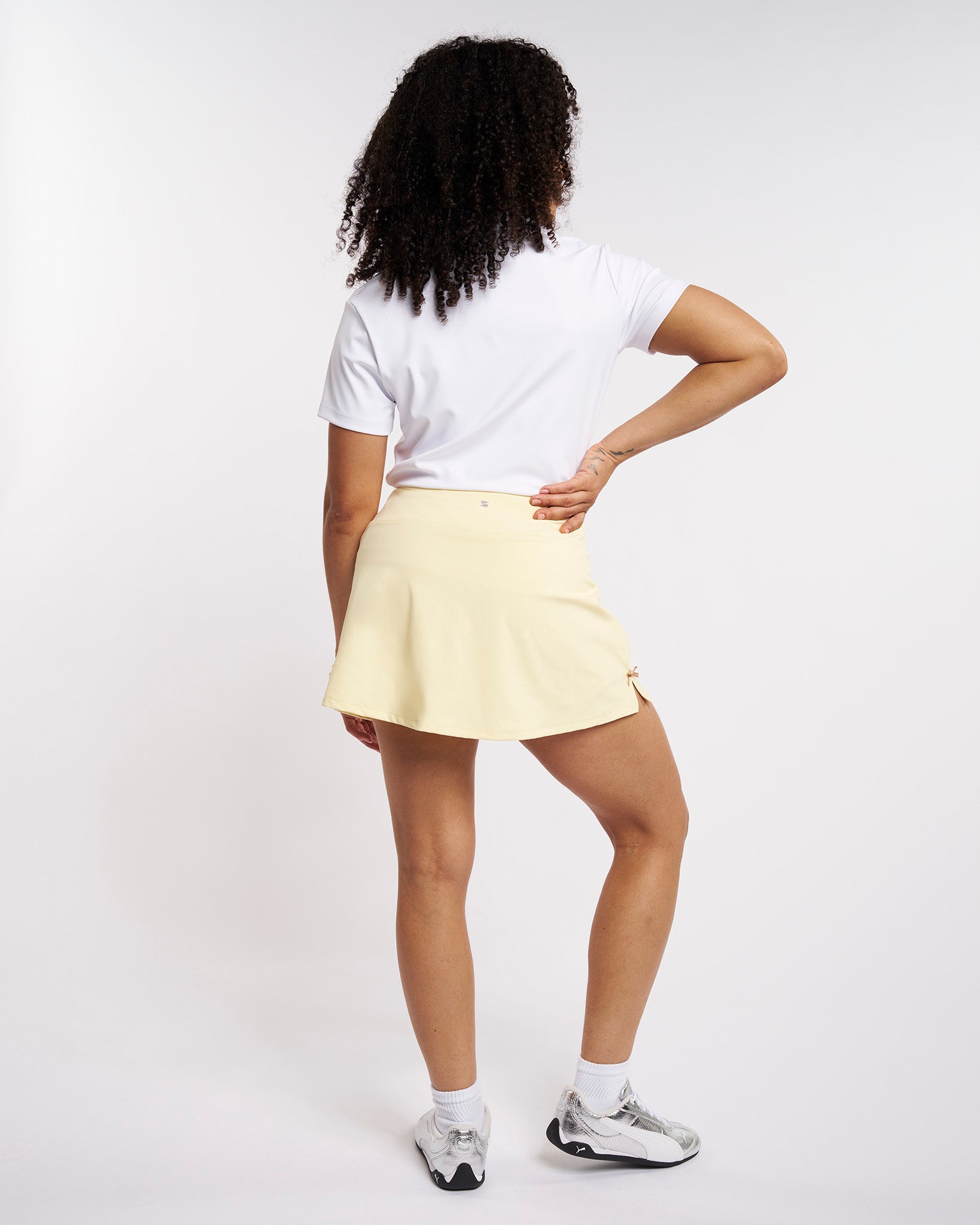 Back view of woman wearing a Lemon Butter high-waisted tennis skirt with a slightly flared silhouette and side bow detail.