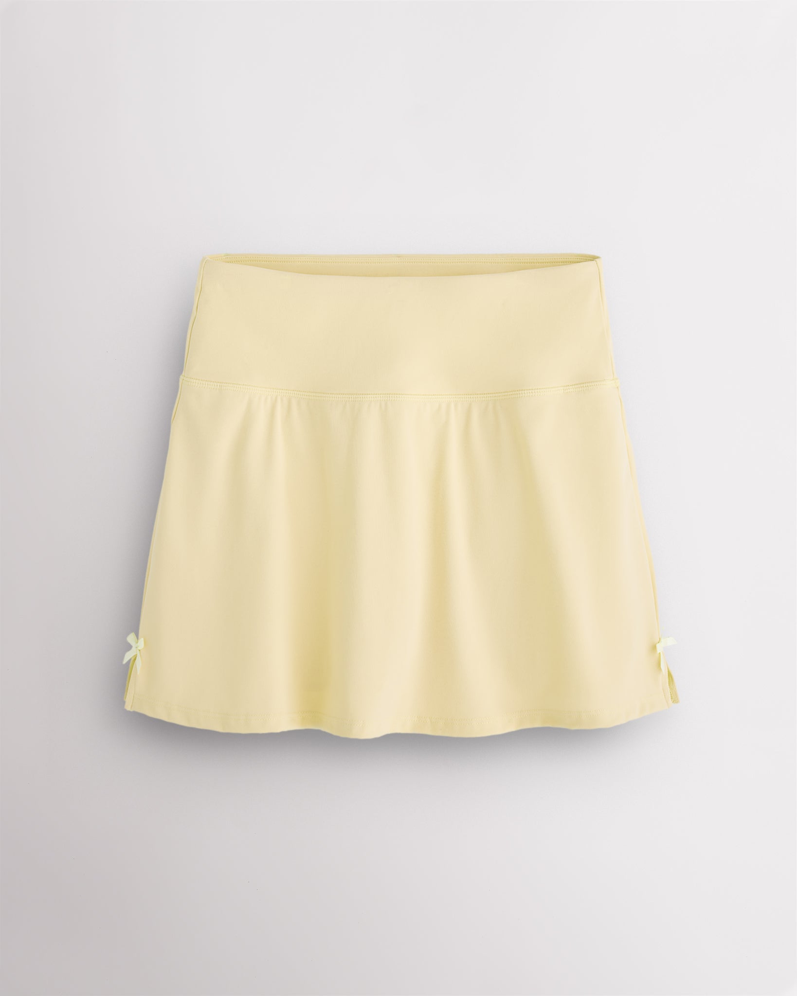 Lemon Butter Stelle classic tennis skirt with a high-waisted fit, slightly flared silhouette, side slits, and bow ribbon details.