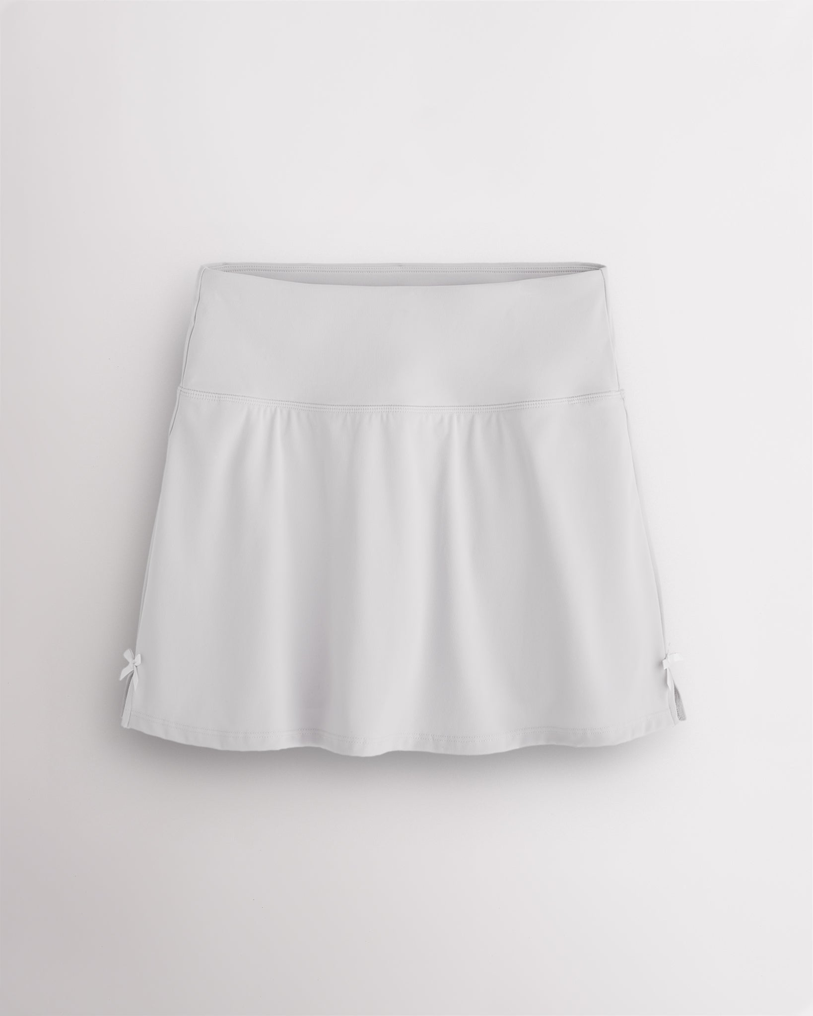 White Stelle classic tennis skirt with a high-waisted fit, slightly flared silhouette, side slits, and bow ribbon details.