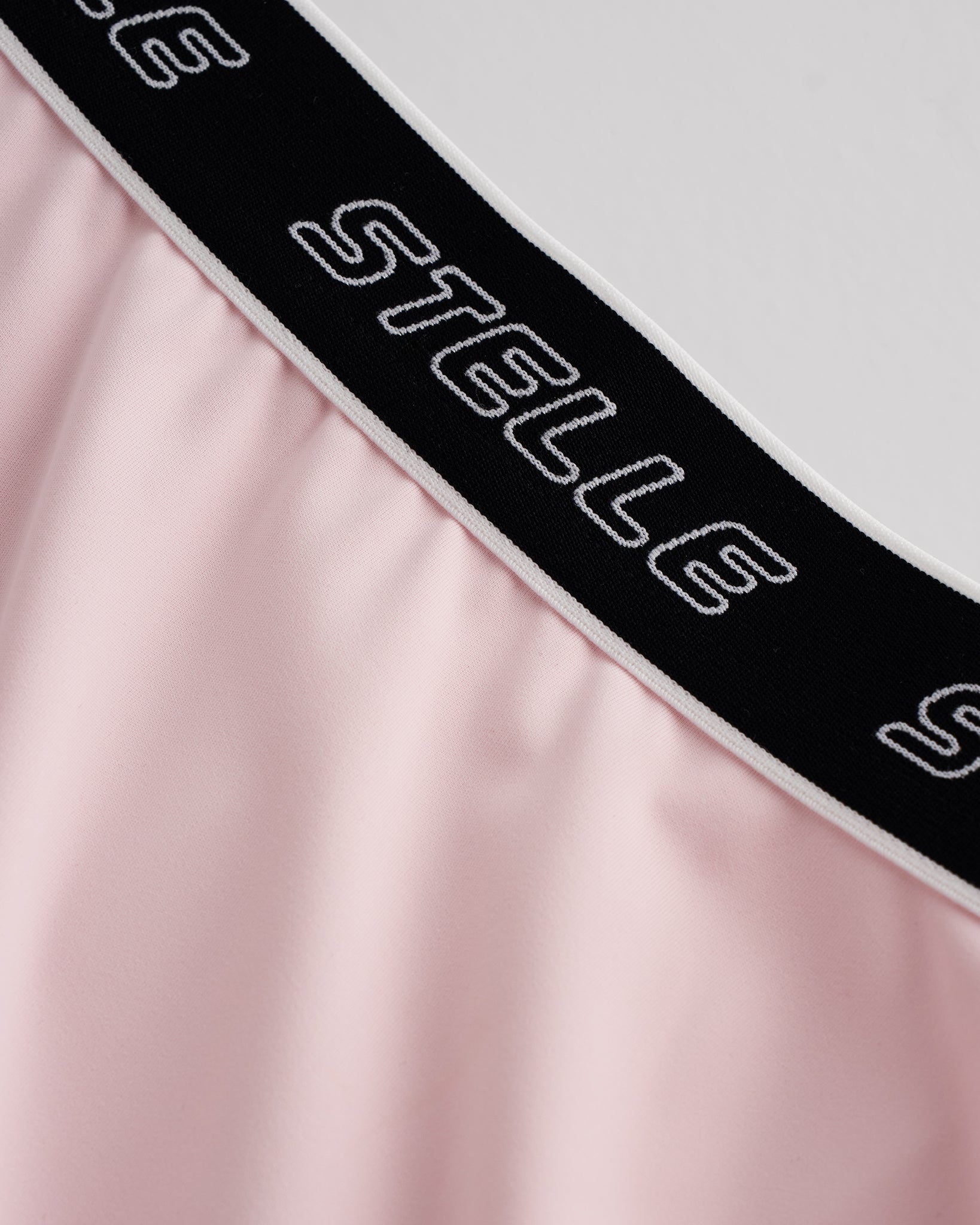 Close-up of ballet pink Stelle tennis skirt showing black logo elastic waistband and soft flared fabric detail.