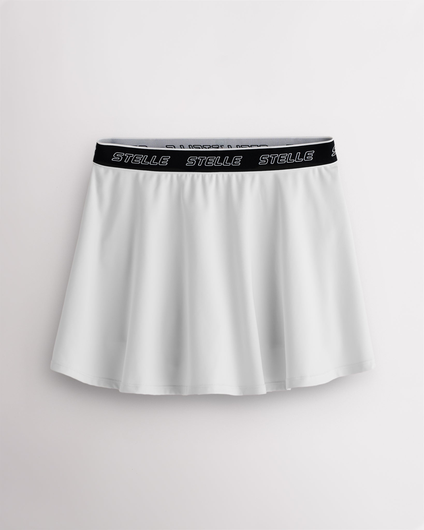 White Stelle tennis skirt with black logo elastic waistband, high-waisted fit, flared skirt, and built-in shorts.