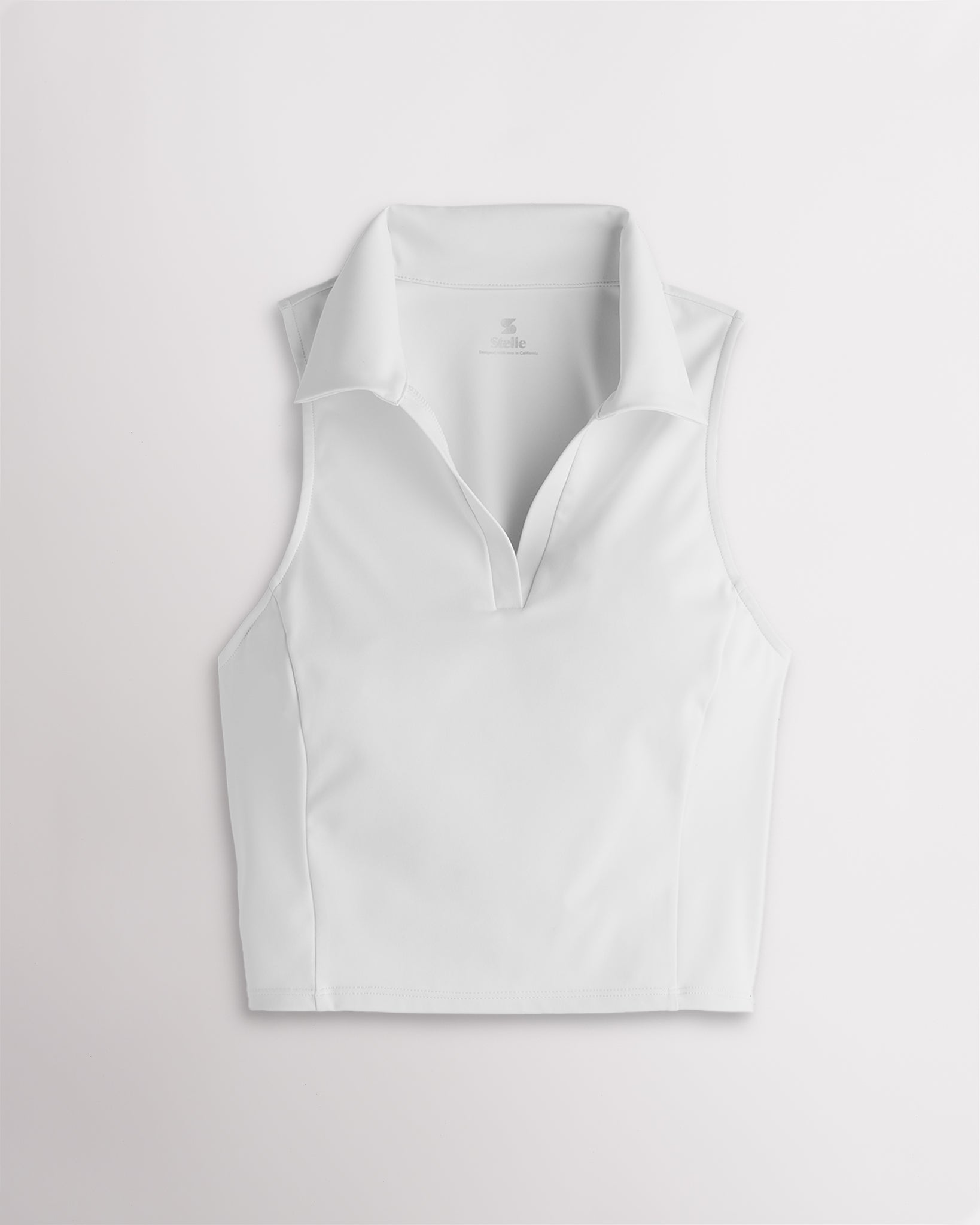 Women’s white fitted cropped polo tank top with a V-neckline, classic collar, sleeveless cut, and contoured seam detailing.