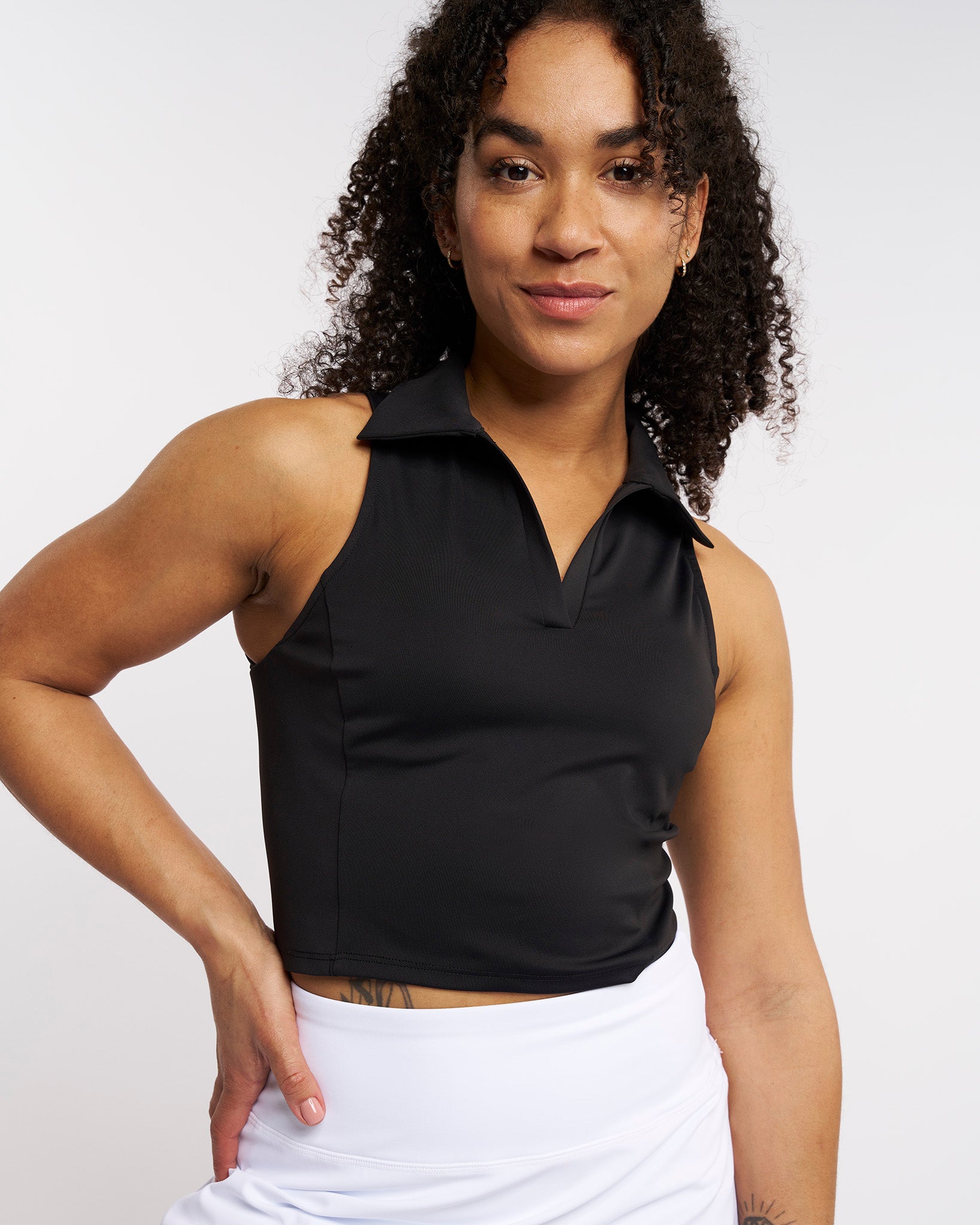 Woman wearing a black fitted cropped polo tank top with a V-neckline, classic collar, and sleeveless design.