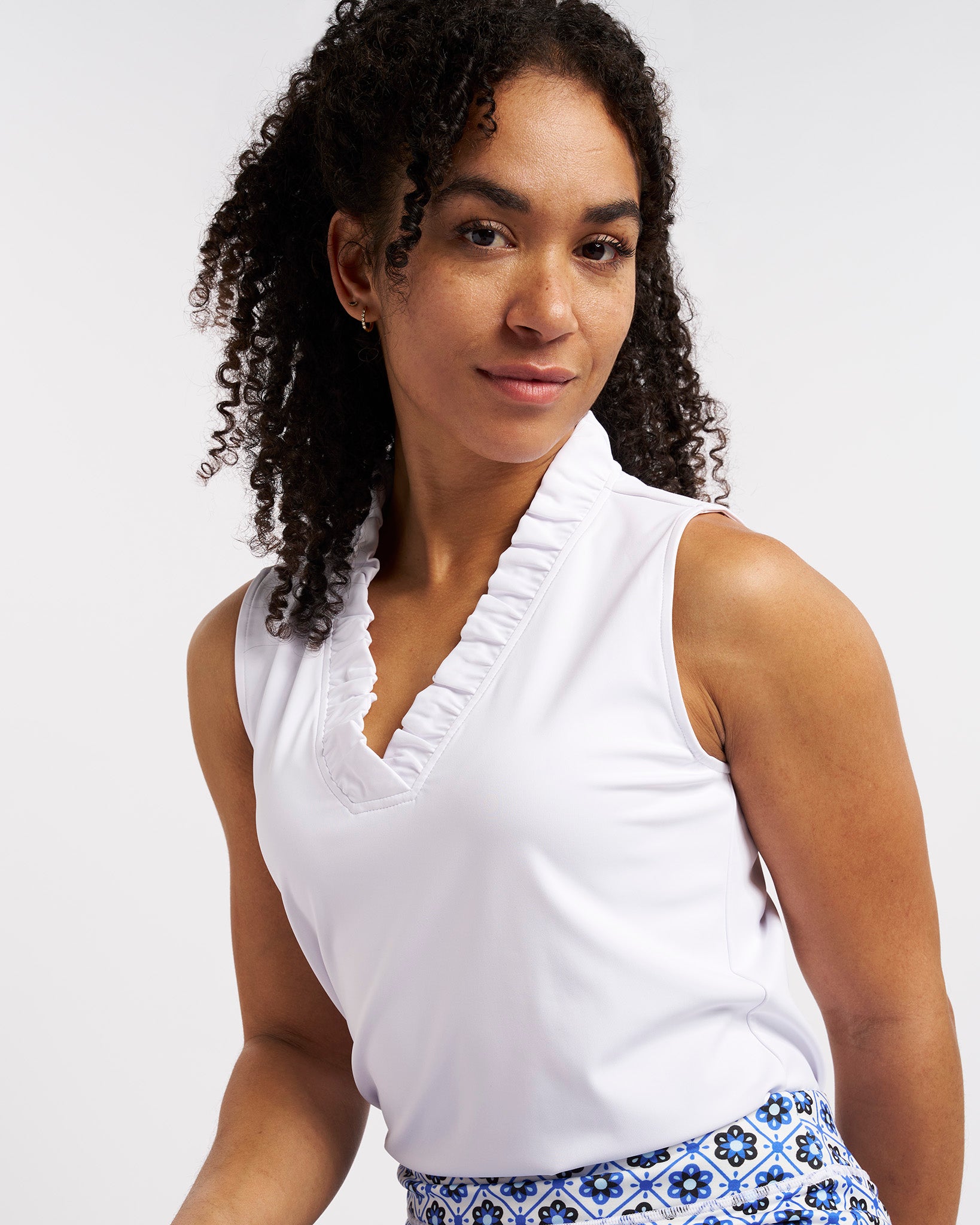 White ruffle V-neck sleeveless polo shirt worn by a woman.
