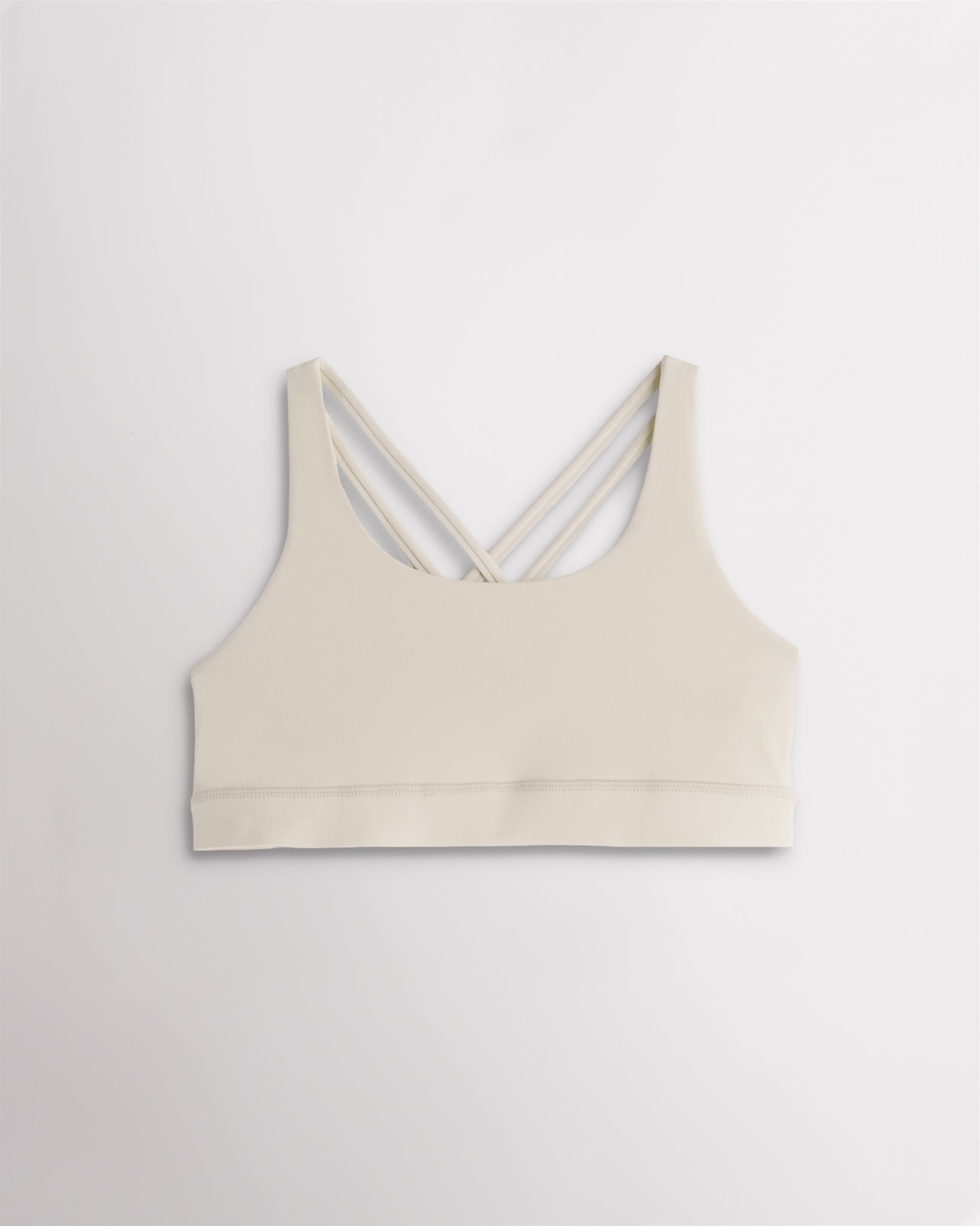 Girls creme sports bra with a scoop neckline, supportive band, and strappy criss-cross back design.
